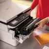 A person is shown replacing the toner cartridge in a Brother printer. Produktbild-Vorschau