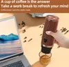 A hand holding a portable espresso machine, brewing coffee into a glass, with a laptop and coffee beans in the background. Produktbild-Vorschau