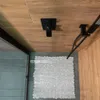A shower stall with a wooden ceiling, a black shower head, and a transparent pebble-shaped bath mat on the floor. Náhľad obrázku produktu