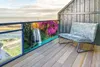 A balcony with a view of the ocean, featuring a chair and a decorative screen with a waterfall and trees. Náhled obrázku produktu
