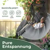 A woman relaxing in a gray hammock chair on a balcony with plants and sunlight. Produktbild-Vorschau