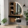 A modern vanity set with a round LED mirror, shelves, and a stool in a room with plants and a window. Voir les images du produit