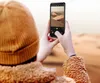 A person in a desert landscape takes a photo of sand dunes with their phone. Produktbild-Vorschau
