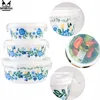 A collage of images showing a set of three glass food containers with floral patterns and their lids, including a close-up of the lid mechanism and a view of one container filled with salad. Produktbild-Vorschau