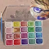 A set of watercolor paints with a brush and a close-up illustration of an eye being painted. Voir les images du produit