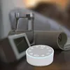 A sound machine is placed on a nightstand next to a glass of water and a clock. Produktbild-Vorschau