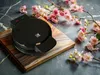 A black waffle maker sits on a wooden board, surrounded by pink cherry blossoms. Náhľad obrázku produktu