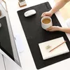 A person's hands holding a mug of tea over a desk mat with a mouse, notebook, pencil, and sharpener. Produktbild-Vorschau