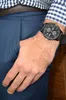 A man's hand with a watch on his wrist is placed in the pocket of his blue pants. He is wearing a blue and white checkered shirt. Podgląd zdjęcia produktu