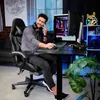 A man is sitting in a gaming chair at a desk with a computer. Produktbild-Vorschau