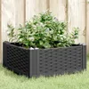 A black woven planter box filled with green plants and white flowers sits on green grass in front of a wooden fence. Produktbild-Vorschau