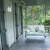 A porch swing with cushions on a wooden porch, with trees in the background. Podgląd zdjęcia produktu