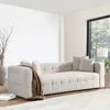 A modern living room with a beige bouclé sofa, a throw blanket, and decorative elements. Voir les images du produit