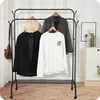 A black metal garment rack with clothes hanging on it, placed in a room with a white wall and wooden floor. Anteprima dell’immagine prodotto