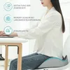 A woman sits at a desk using a laptop, with a seat cushion on her chair. Text overlays describe the cushion's features. Produktbild-Vorschau