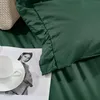 A close-up of a green duvet cover with a ruffled edge, a white teacup and saucer on a magazine featuring a woman's portrait, and a beige knitted item in the background. Podgląd zdjęcia produktu
