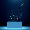 An Adidas exercise bike is displayed on a light blue pedestal against a dark blue background, with dramatic lighting. Produktbild-Vorschau