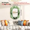 A decorative mirror clock is displayed on a wall above a sofa with decorative pillows. Produktbild-Vorschau