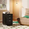 A black filing cabinet with three drawers sits on a patterned rug next to a plush chair. Anteprima dell’immagine prodotto