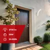 An outdoor wall lamp is mounted on a wall next to a wooden door, with plants and bushes in the foreground. Anteprima dell’immagine prodotto