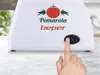 A close-up of a white electric tomato press with branding and a finger pressing the power button. Produktbild-Vorschau