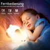 A young girl sleeping in bed next to a glowing bunny-shaped night light. Produktbild-Vorschau