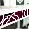 Close-up view of a white desk with a decorative burgundy and white patterned trim. Produktbild-Vorschau