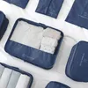Several blue fabric packing cubes are laid out on a white surface, with one cube open and filled with folded clothes. Anteprima dell’immagine prodotto