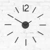 A modern, frameless wall clock with black hour markers and hands, mounted on a white brick wall. Produktbild-Vorschau