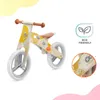 A wooden balance bike with yellow and white swirl pattern, on a white background with colorful abstract shapes. Náhľad obrázku produktu