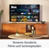 A television displaying a streaming interface, placed on a wooden media console in a living room setting. Produktbild-Vorschau