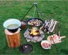 An outdoor cooking setup with a campfire, tripod, cooking pots, and ingredients. Produktbild-Vorschau