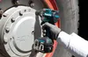 A person wearing gloves is using a Makita cordless impact wrench to tighten a bolt on a large wheel hub. Anteprima dell’immagine prodotto