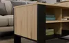 A close-up view of a modern coffee table with a wood-effect finish and black accents, showing its shelving and part of a sofa in the background. Voir les images du produit