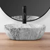 A close-up shot of a marble sink with a black faucet in front of a round mirror. Produktbild-Vorschau
