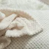 A close-up view of a soft, cream-colored blanket with a textured pattern. Produktbild-Vorschau
