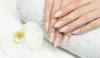 A close-up shot of a person's hands with a French manicure, resting on a white towel next to a white orchid. Náhled obrázku produktu