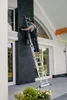 A man is cleaning a dark-colored chimney on a house exterior while standing on a multi-purpose ladder. Produktbild-Vorschau