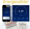 A smartphone displaying an energy meter app next to a miniature house model and stacks of coins, overlaid on architectural plans. Náhled obrázku produktu
