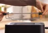 A person is holding a chrome rack above a black toaster. Voir les images du produit