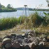 A tripod grill set up near a campfire pit by a lake. Produktbild-Vorschau