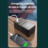 A black 12-port USB charging station is shown on a wooden desk, with a smartphone connected to it. Náhled obrázku produktu