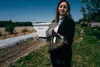 A woman is sowing seeds in a field using a hand-held spreader. Produktbild-Vorschau