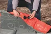 A person is shown kneeling and interacting with an inflatable mattress, possibly preparing it for use or packing it. Podgląd zdjęcia produktu