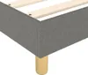 A close-up view of the corner of a dark gray fabric box spring bed frame with wooden legs. Produktbild-Vorschau