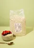 A large bag of oats stands behind a bowl of oatmeal topped with berries, with a spoon in the foreground. Produktbild-Vorschau