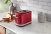 A red toaster sits on a kitchen counter next to sliced bread, with a vase and a canister in the background. Anteprima dell’immagine prodotto