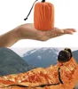 A person is wrapped in an orange emergency sleeping bag in a mountainous landscape. Podgląd zdjęcia produktu