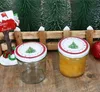Two Christmas-themed jars are displayed on a wooden surface, with miniature Christmas trees and a Santa mailbox in the background. Produktbild-Vorschau
