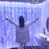 A person stands with their arms outstretched in front of a wall covered in blue LED string lights. Náhled obrázku produktu